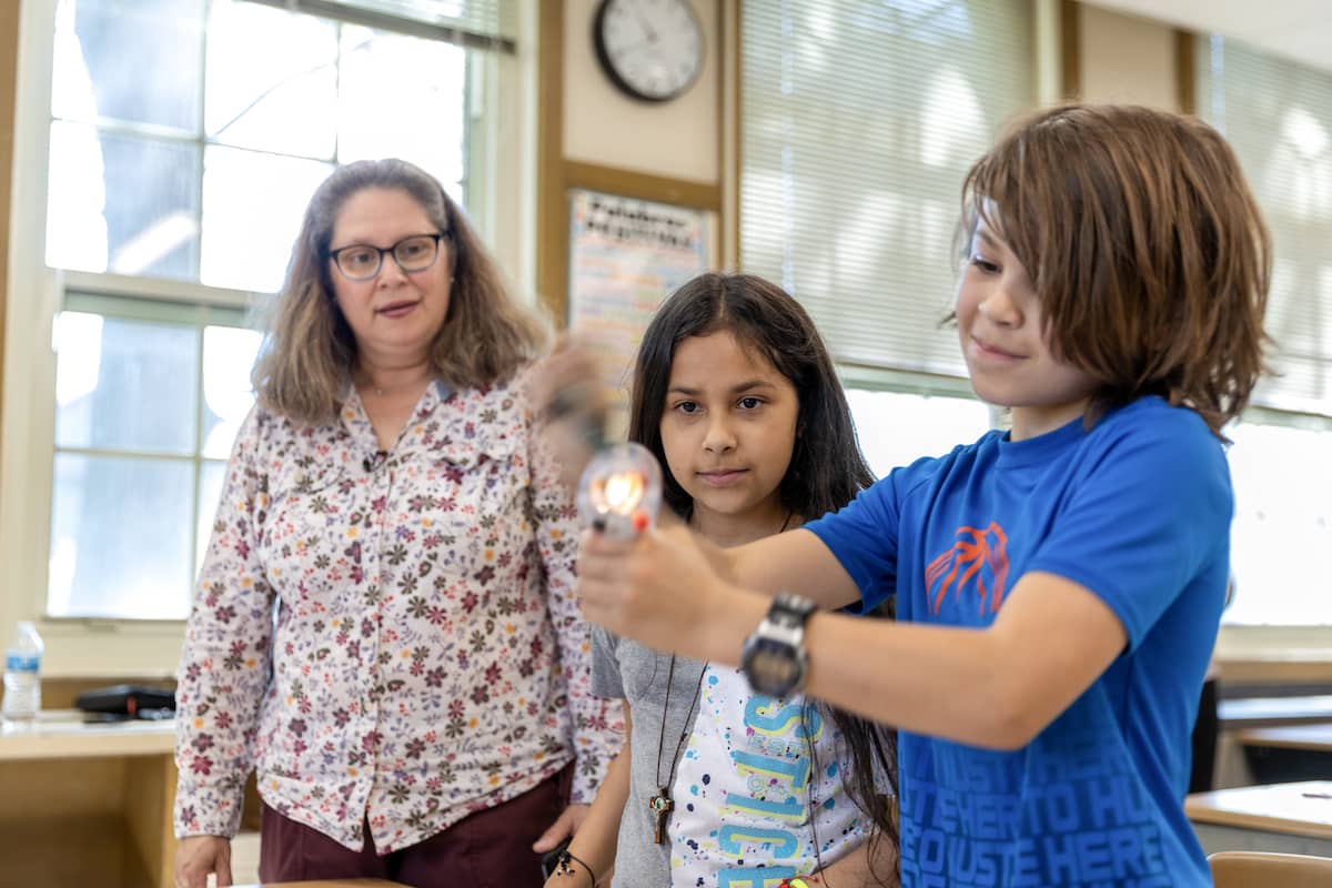 Students engaging with hand-crank flashlight as teacher observes